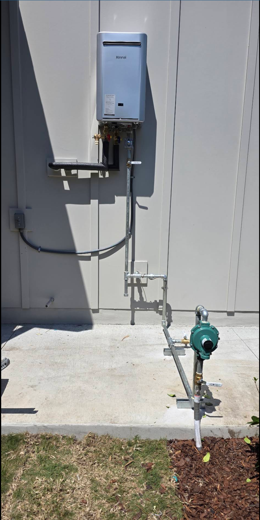 Outdoor tankless water heater with a neatly routed gas line, regulator and labeled shutoff valves along the side of a home